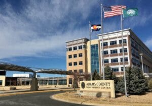 The Adams County Government Center is a large building with the Colorado and US flags flown outside.